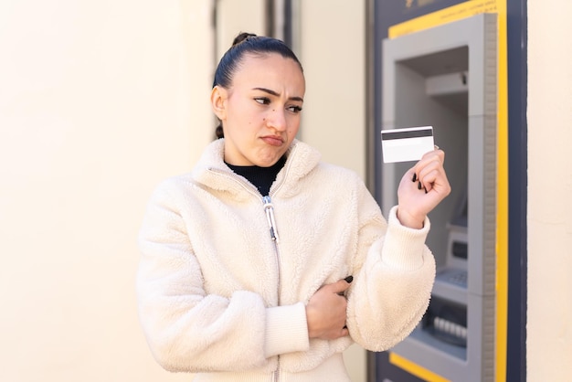 Young moroccan girl holding a credit card at outdoors with sad expression