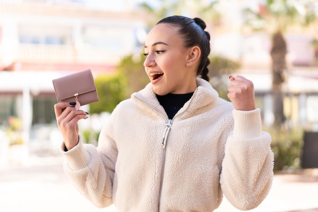 Young moroccan girl holding a wallet at outdoors celebrating a victory