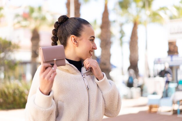 Young moroccan girl holding a wallet at outdoors thinking an idea and looking side