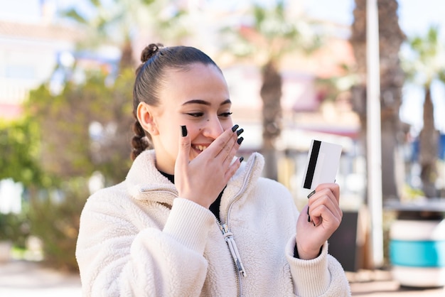 Young moroccan girl at outdoors holding a credit card with surprised expression