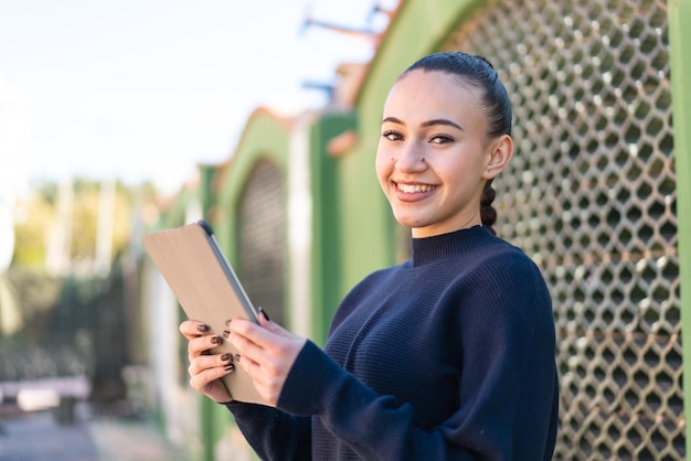 Young moroccan girl at outdoors holding a tablet with happy expression