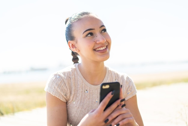 Young moroccan girl at outdoors using mobile phone and looking up