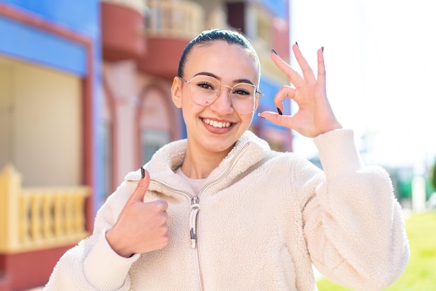 Young moroccan girl at outdoors With glasses and doing OK sign