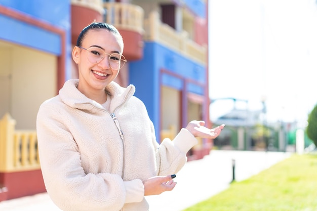 Young moroccan girl at outdoors With glasses and presenting something