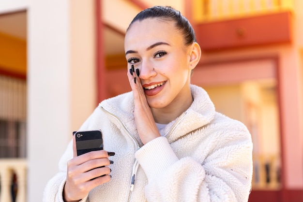 Young moroccan girl using mobile phone at outdoors whispering something