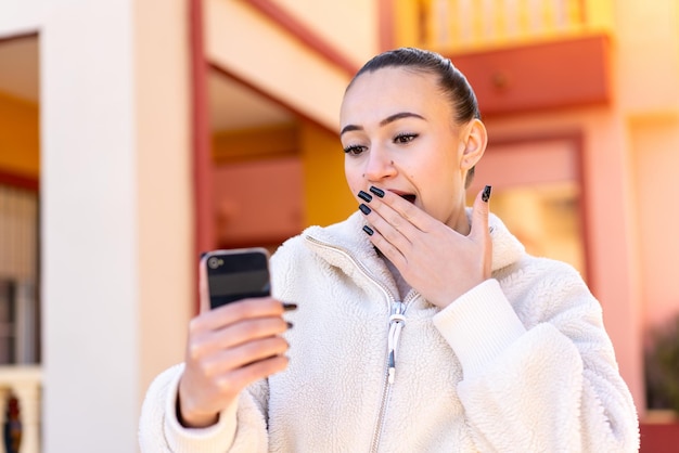 Young moroccan girl using mobile phone at outdoors with surprise and shocked facial expression