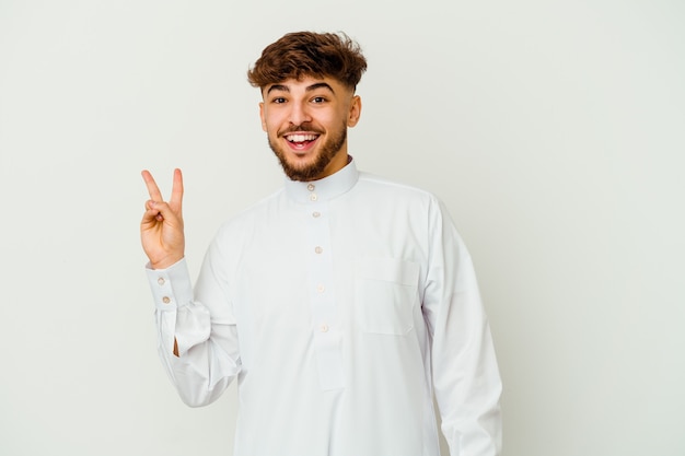 Young Moroccan man wearing a typical arab clothes isolated on white wall joyful and carefree showing a peace symbol with fingers.