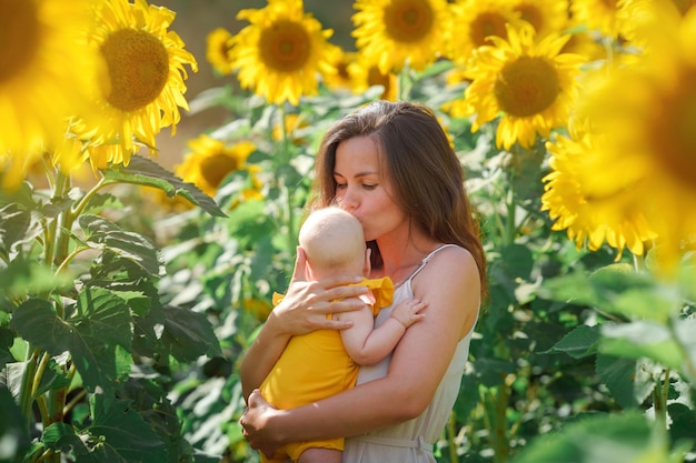 Young mother and baby girl happy together, hugging in nature in a field of yellow sunflowers.