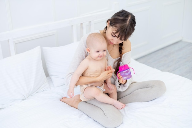 A young mother feeds a baby from a bottle with milk or water in her arms love mother's care for the baby happy motherhood the concept of baby food