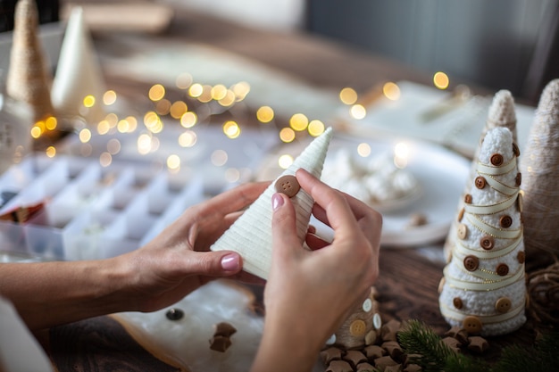 Young mother helping to daughter for wrapping foam cone with string or yarn and crafting different size of Christmas Trees for table decoration. Concept of preparation for Festive season and party.