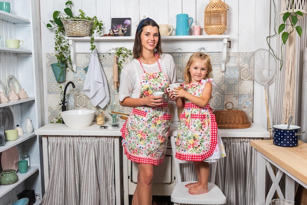 Young mother and her daughter are cooking in the kitchen in beautiful aprons