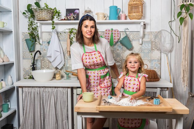 Young mother and her daughter are cooking in the kitchen in beautiful aprons