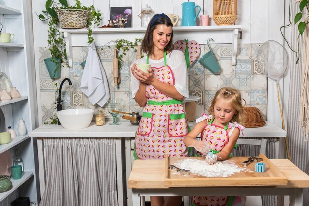 Young mother and her daughter are cooking in the kitchen in beautiful aprons