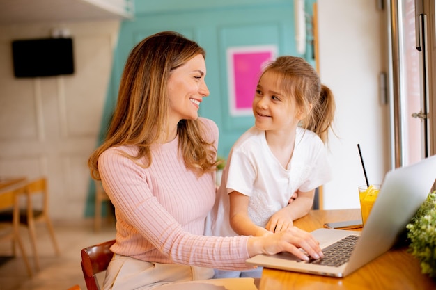 Young mother and her daughter working on laptop and drinking fresh orange juice in the cafe