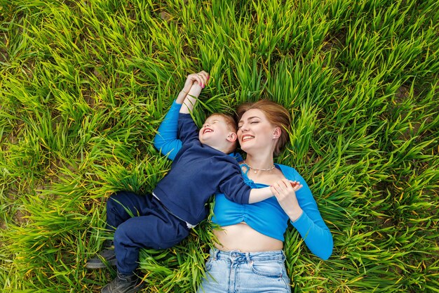 A young mother and her son are lying in the green grass Family relations of mother and child A happy family