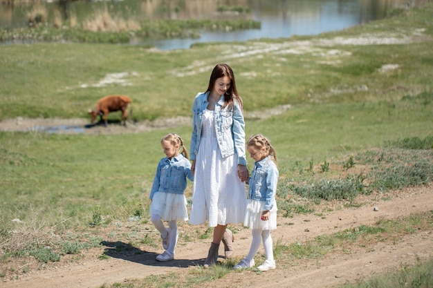 Young mother and her twin daughters are walking along a path in the village