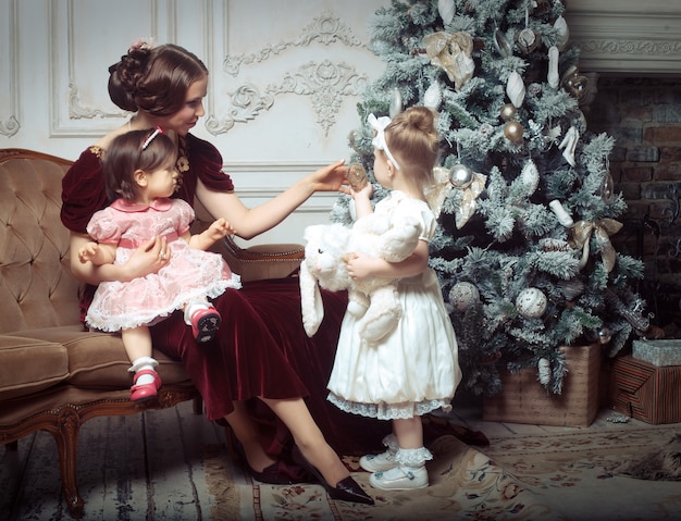 Young mother and her two little daughters near Christmas tree