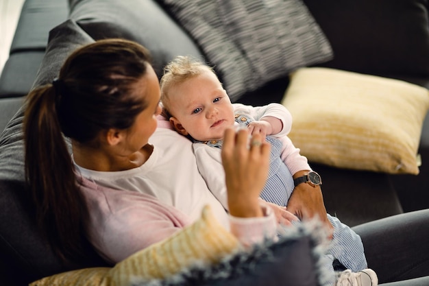 Young mother holding her baby boy while sitting on the sofa at home