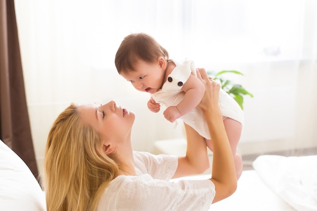 Young mother holding her newborn kid. Happy mom nursing baby. Woman and new born girl together in a white bedroom at home. Mother breast feeding baby. Family lifestyle