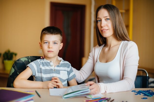 A young mother is doing homework with her son at home. Parents and training