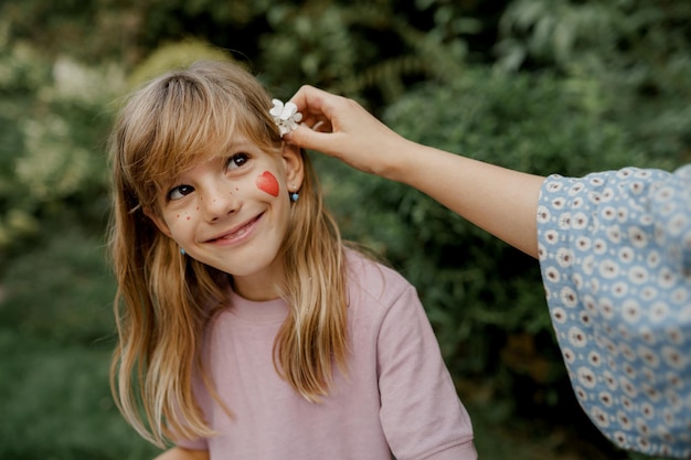 Young mother is putting flower on hair of her child in the garden. Family time.