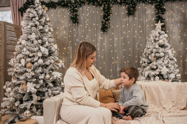 A young mother is sitting on the sofa and talking to her son Todd in the room near the Christmas tree