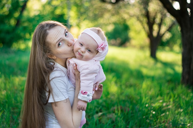 Young mother kissing baby on nature park. Walk in Park with baby.