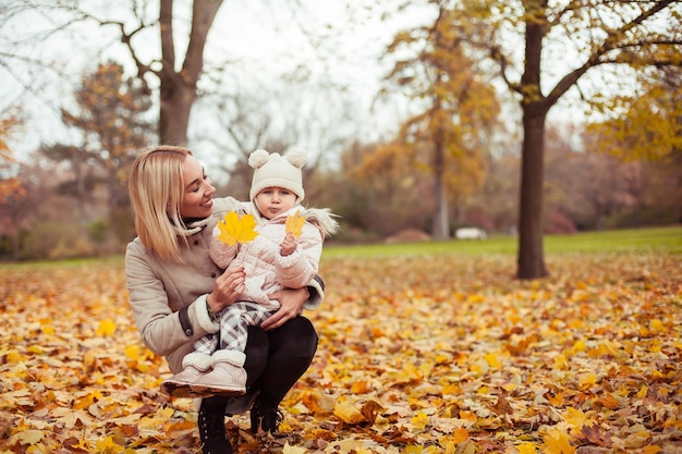 Young mother and little daughter walk in the autumn. Mom and daughter play. Warm winter. Bright autumn. Cozy.