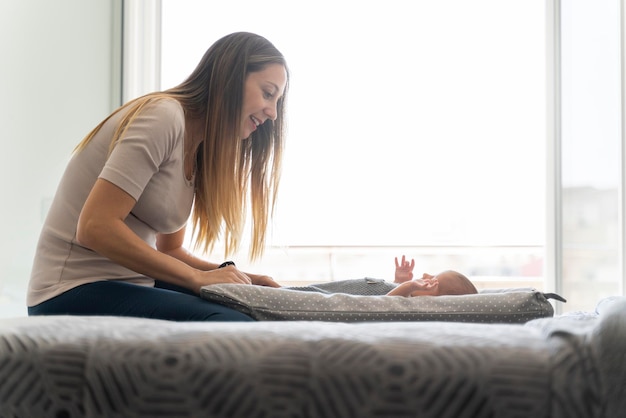 Young mother looking at her newborn baby on the bed in the bedroom near the window