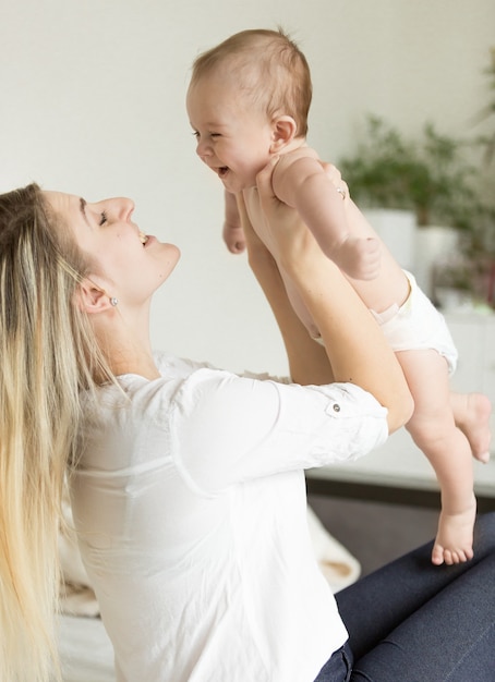 Young mother lying on bed and holding her 6 month son on hands