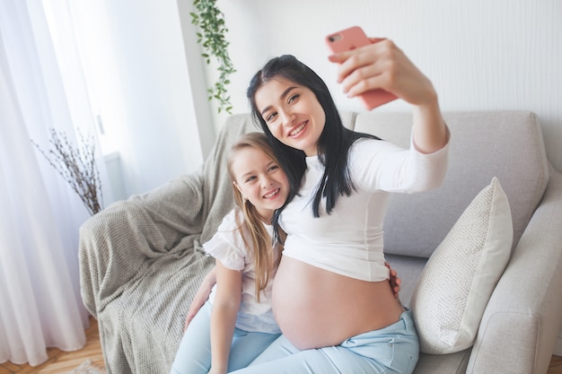 Young mother making selfie with her little daughter. Woman expecting baby. Happy family indoor.