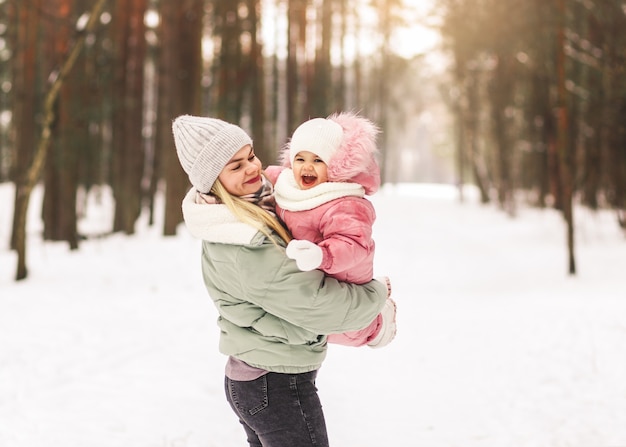 Young mother plays with her little daughter in winter in the park, holds in her arms and circles