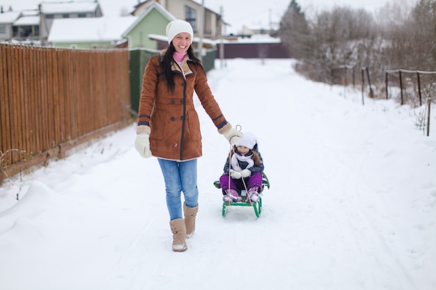 Young mother rolls her little cute daughters on a sled in winter day