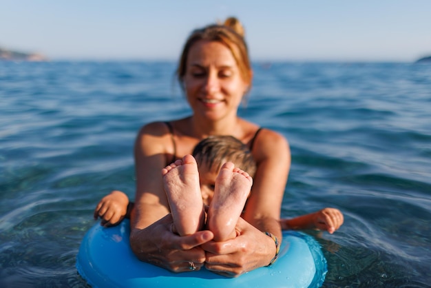 A young mother shows the legs and arms of her baby who is sitting in an inflatable ring in the sea