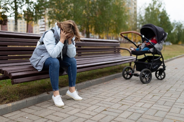 A young mother sits on a bench upset next to a baby stroller concept of postpartum depression