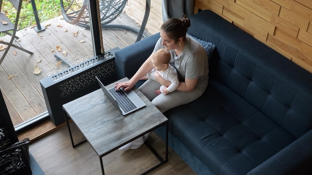 Young mother sits holding baby on lap and works at laptop