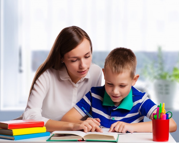 Young mother sitting at a table at home helping her small son with his homework from school