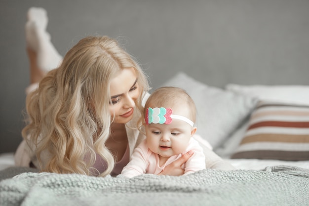 Young mother taking care of her little baby girl. Beautiful mom and her daughter indoors in the bedroom. Loving family. Attractive mum holding her child.