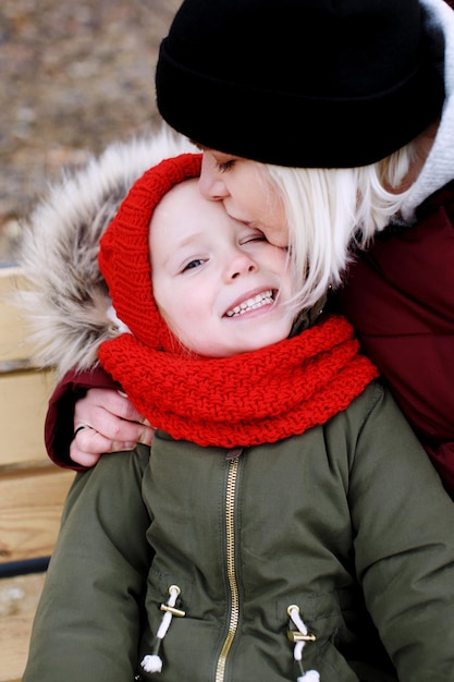 Young mother talking to her cute little daughter outdoors sitting together in warm clothes