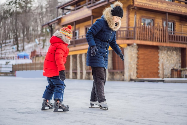 Young mother teaching her little son ice skating at outdoor skating rink Family enjoy winter on icerink outdoors