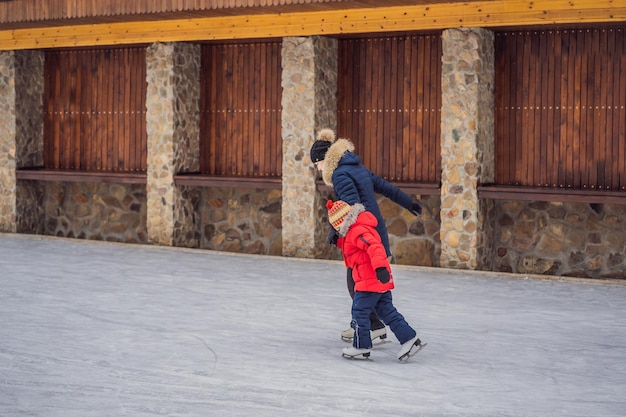 Young mother teaching her little son ice skating at outdoor skating rink Family enjoy winter on icerink outdoors