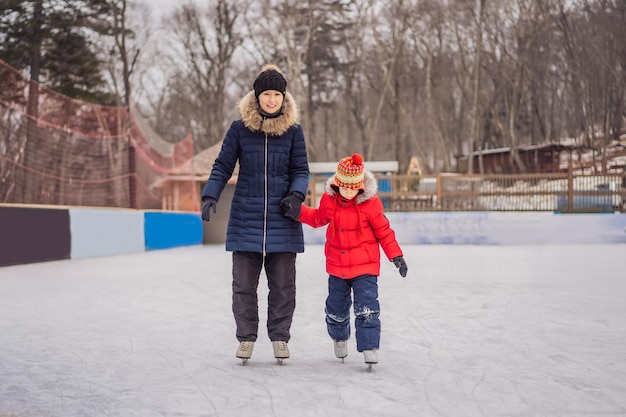 Young mother teaching her little son ice skating at outdoor skating rink Family enjoy winter on icerink outdoors