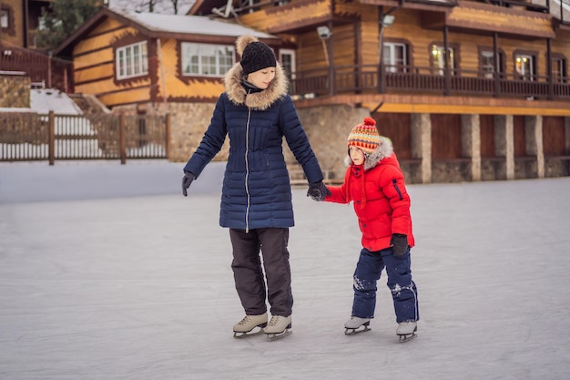 Young mother teaching her little son ice skating at outdoor skating rink Family enjoy winter on icerink outdoors