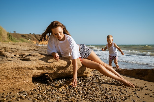 Young mother watches her son play by the sea on a sunny summer day