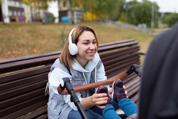 A young mother while walking with a small child in a stroller in headphones plays with him stroking