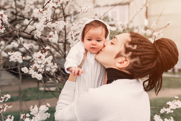 Young mother with adorable daughter in park with blossom tree. Happy mother and child