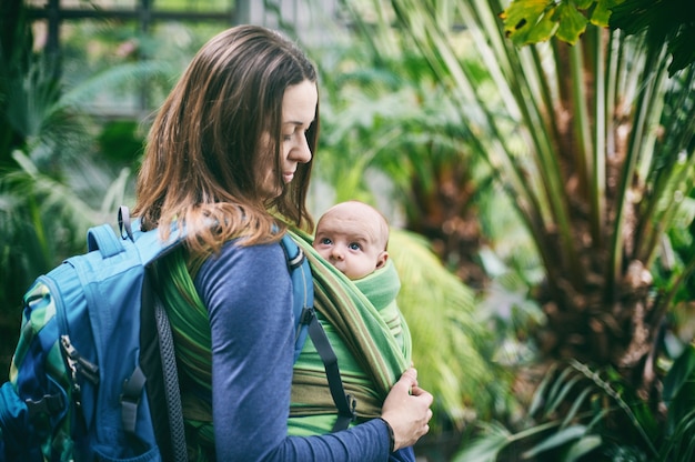 A young mother with a baby in a sling is walking in the jungle