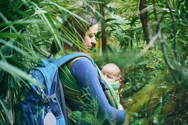 A young mother with a baby in a sling is walking in the jungle