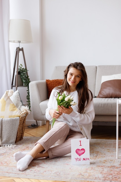 Young mother with a bouquet of tulips and a postcard in the living room