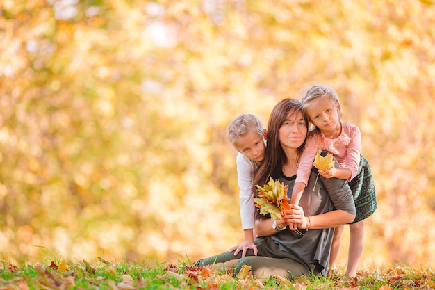 Young mother with cute little girls in autumn park on sunny day. Family enjoy warm weather at september day